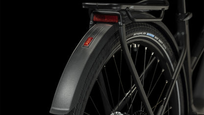 Nahaufnahme des Hinterrads eines CUBE Touring Hybrid Pro 625 black'n'metal Trapeze 2024, wobei das Schutzblech, der Reifen, die Speichen, der Gepäckträger und der rote Reflektor vor einem schwarzen Hintergrund hervorgehoben werden.