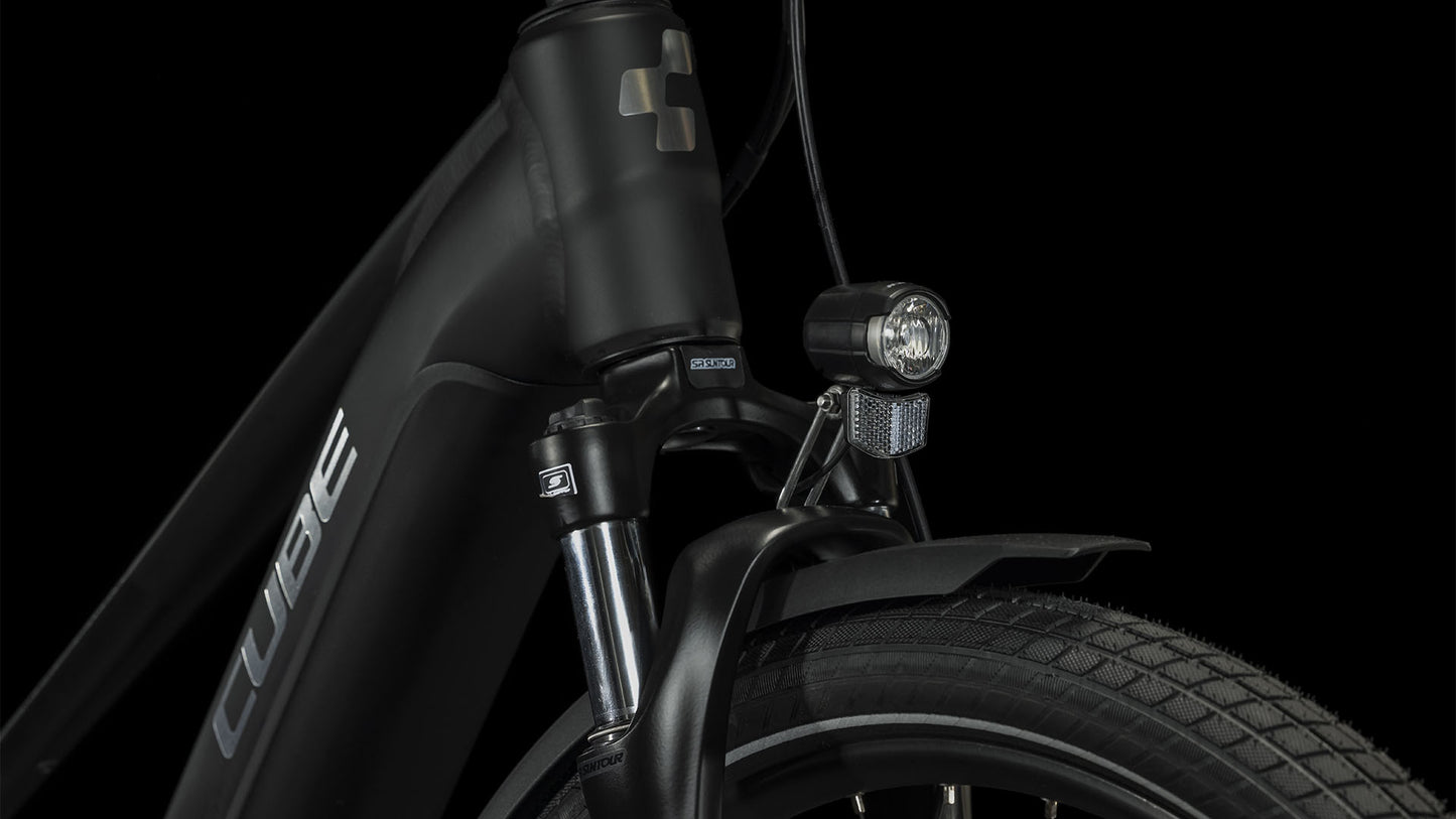 Nahaufnahme der Vorderseite des CUBE Touring Hybrid Pro 625 black'n'metal Trapeze 2024 mit dem Cube-Logo auf dem Steuerrohr, dem Scheinwerfer, dem Reifen mit dickem Profil und einem Teil des Schutzblechs - angetrieben von einem Bosch Performance Motor - vor schwarzem Hintergrund.