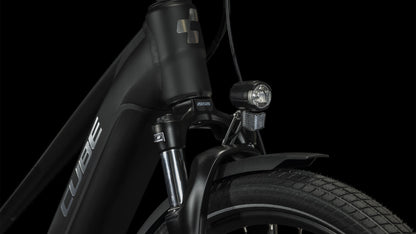 Nahaufnahme der Vorderseite des CUBE Touring Hybrid Pro 625 black'n'metal Trapeze 2024 mit dem Cube-Logo auf dem Steuerrohr, dem Scheinwerfer, dem Reifen mit dickem Profil und einem Teil des Schutzblechs - angetrieben von einem Bosch Performance Motor - vor schwarzem Hintergrund.