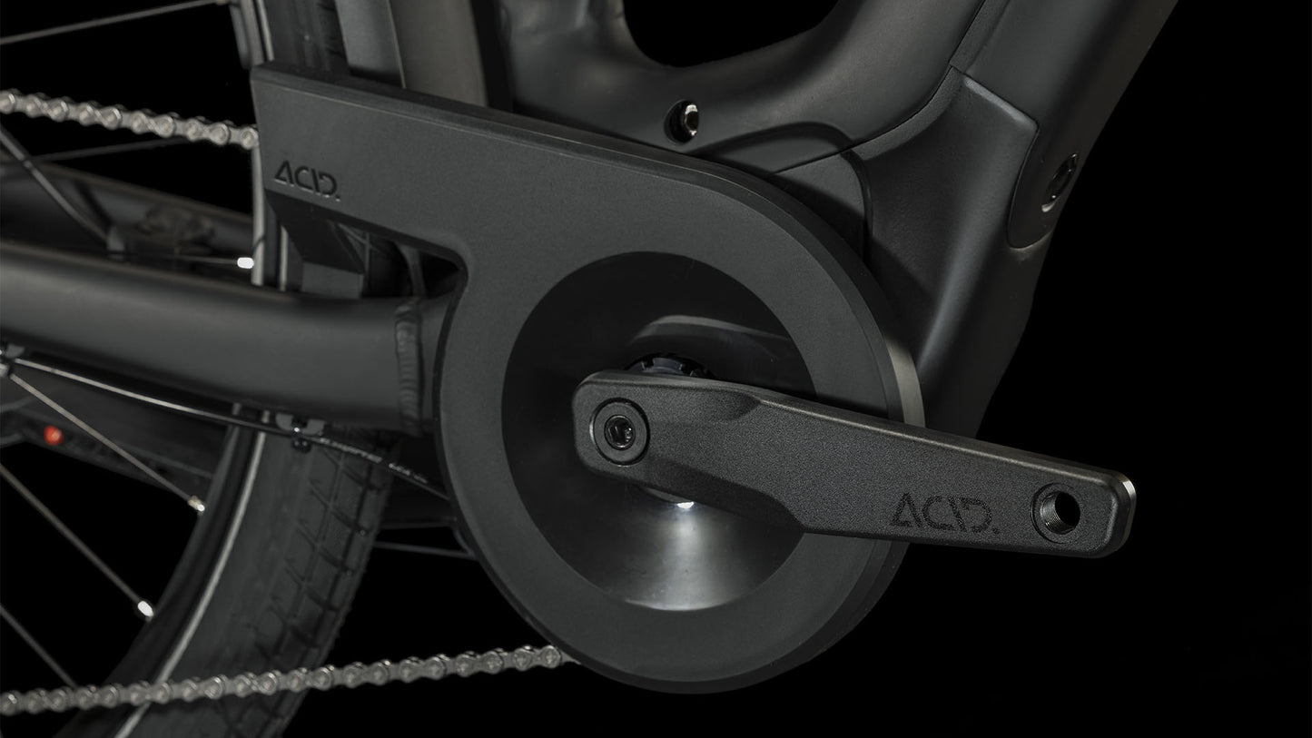 Nahaufnahme des schwarzen Kurbelarms und Kettenschutzes des CUBE Touring Hybrid Pro 625 black'n'metal Trapeze 2024 mit ACID-Logo, Bosch Performance Motor und Shimano 11-Gang Schaltung vor einem dunklen Hintergrund, der das Hinterrad und die Kette hervorhebt.