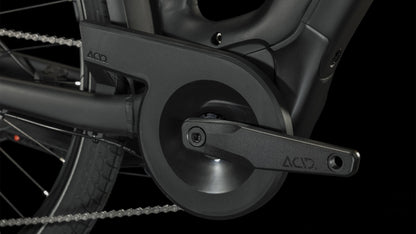 Nahaufnahme des schwarzen Kurbelarms und Kettenschutzes des CUBE Touring Hybrid Pro 625 black'n'metal Trapeze 2024 mit ACID-Logo, Bosch Performance Motor und Shimano 11-Gang Schaltung vor einem dunklen Hintergrund, der das Hinterrad und die Kette hervorhebt.