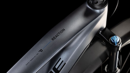 Nahaufnahme des CUBE Reaction Hybrid Pro 800 Allroad metallicgrau-schwarzen 2025-Rahmens mit REACTION-Schriftzug, einem dezenten blauen Akzent und Shimano XT-Vorderradaufhängung vor schwarzem Hintergrund.