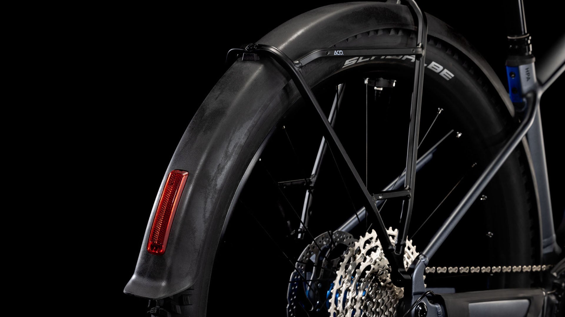 Nahaufnahme des Hinterrads des CUBE Reaction Hybrid Pro 800 Allroad metallicgrey'n'black 2025 mit Schaltkassette, Shimano XT-Teilen, schwarzem Schutzblech mit rotem Reflektor und SCHWALBE-Reifenbranding vor schwarzem Hintergrund.