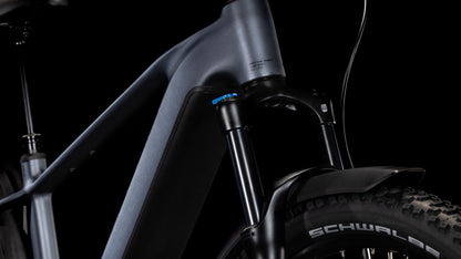 Nahaufnahme des Cube Reaction Hybrid Pro 800 Allroad metallicgrey'n'black 2025 von CUBE, die den modernen Rahmen, die Federgabel, die dicken Schwalbe-Reifen und die hydraulischen Shimano XT-Scheibenbremsen vor einem schwarzen Hintergrund hervorhebt.
