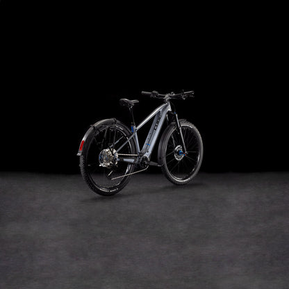 Das CUBE Reaction Hybrid Pro 800 Allroad metallicgrey'n'black 2025, ein modernes E-Bike mit dicken Reifen, Schutzblechen und hydraulischen Scheibenbremsen, wird von hinten links auf dunklem Hintergrund gezeigt.