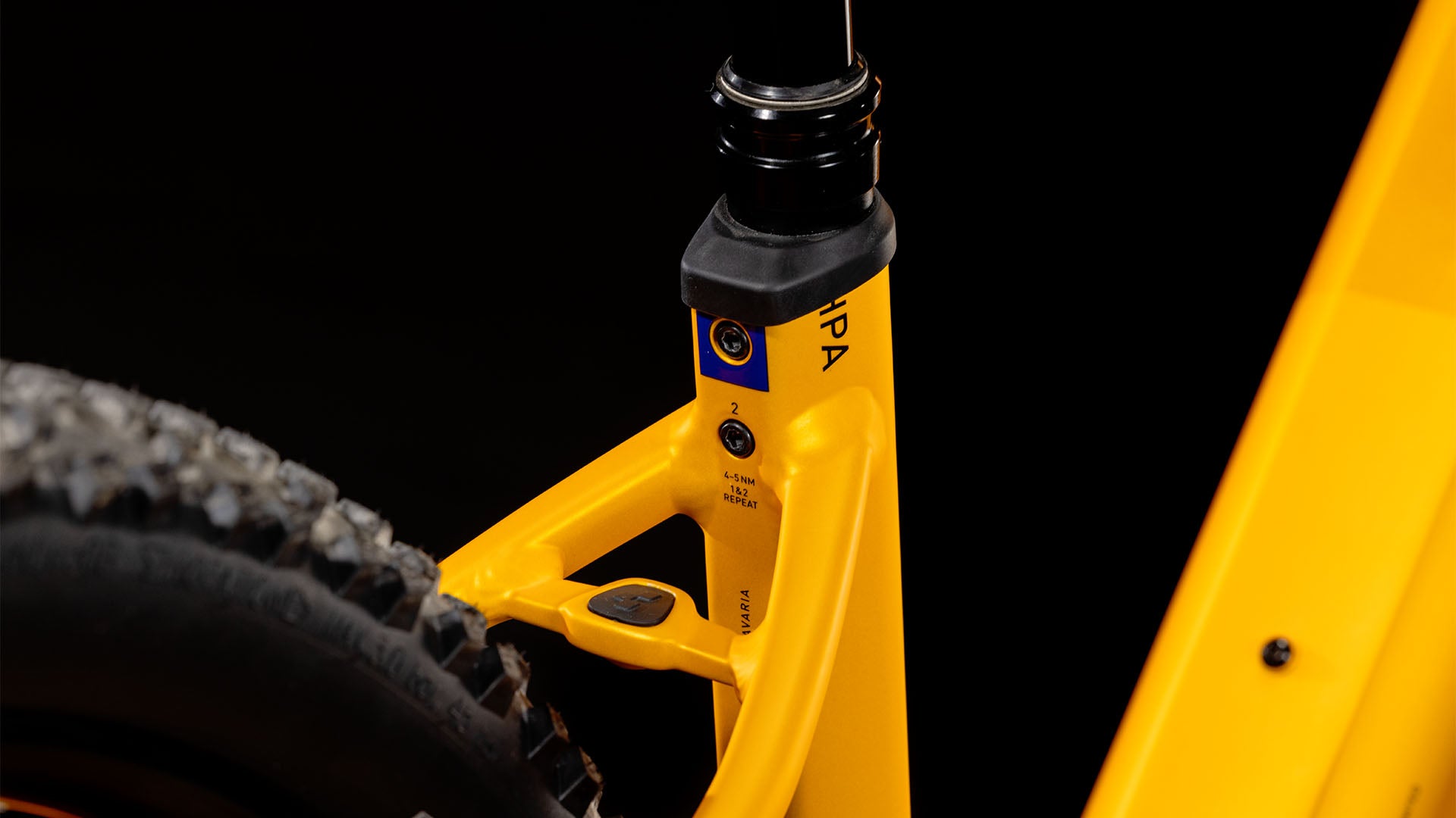 Nahaufnahme des CUBE Reaction Hybrid SLX 800 spectraorange´n´violet Easy Entry 2025-Rahmens mit Hervorhebung des Hinterrads, des Sattelrohrs, des Bosch CX-Motors, des kleinen Bedienfelds und des robusten Reifenprofils vor einem schwarzen Hintergrund.