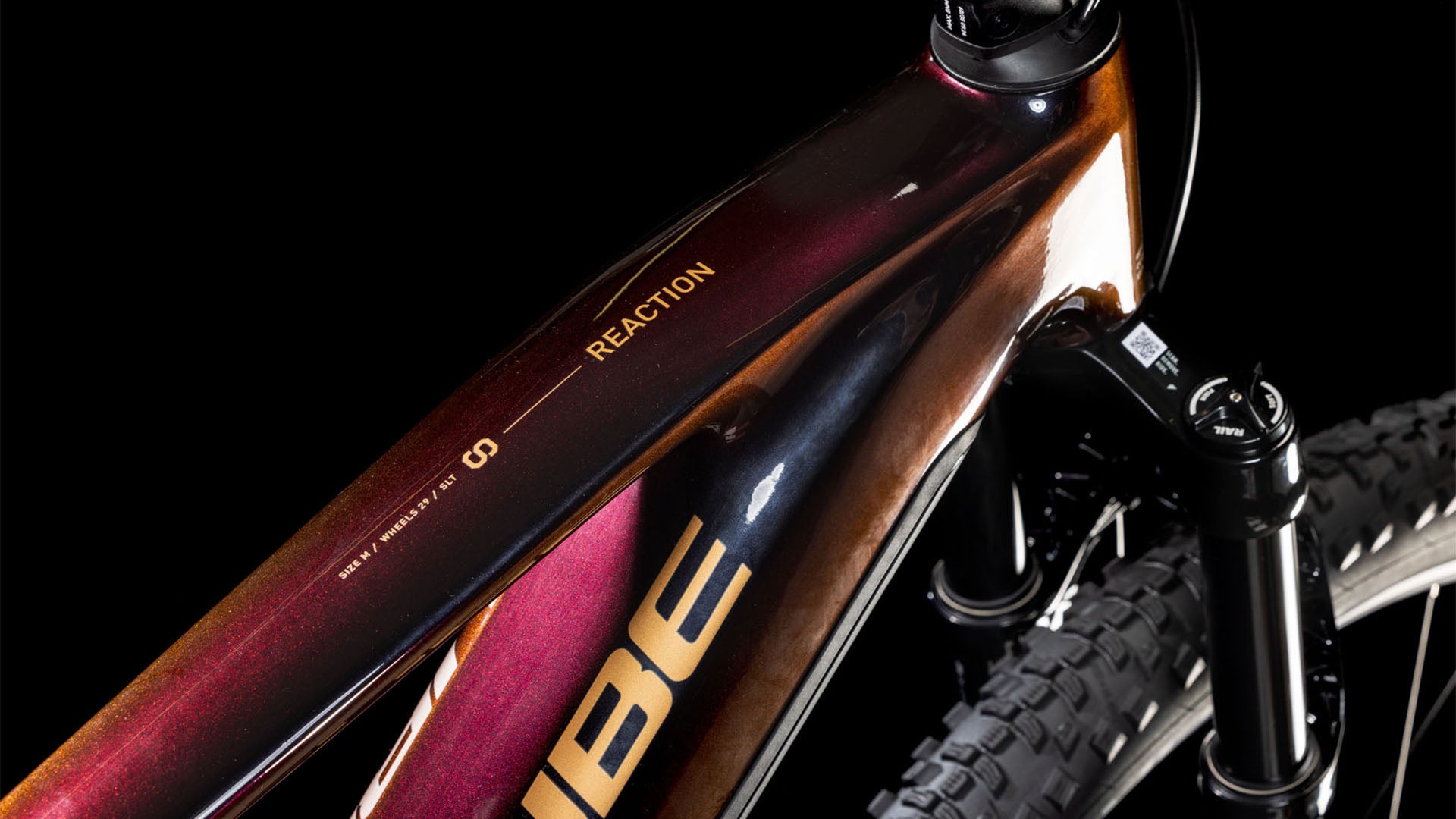 Nahaufnahme des Cube Reaction Hybrid SLT 800 solareclipse'n'bronze 2025 Rahmens, die das Oberrohr mit CUBE-Branding und ein glänzendes dunkelrot-braunes Gradientenfinish zeigt. Sichtbar: ein Teil des Vorderrads, der Gabel und des integrierten PowerTube-Akkus.