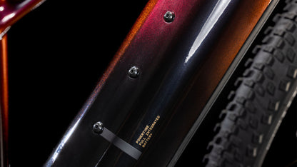 Nahaufnahme des CUBE Reaction Hybrid SLT 800 solareclipse'n'bronze 2025 Rahmens mit metallisch rot-schwarzem Farbverlauf, drei Befestigungsschrauben, Bosch CX Motor und Teilbereifung vor dunklem Hintergrund sichtbar; kleiner Text auf dem Rahmen aufgedruckt.