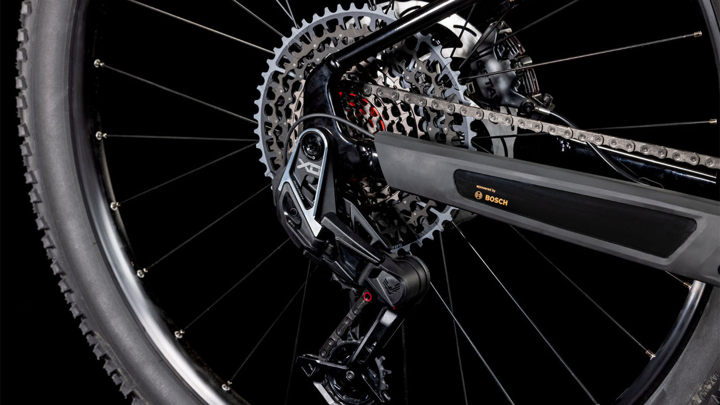 Nahaufnahme des Hinterrads des CUBE Reaction Hybrid SLT 800 solareclipse'n'bronze 2025, der SRAM XO Eagle-Schaltung, der Kette, des Umwerfers und des Bosch CX-Motors vor einem schwarzen Hintergrund.