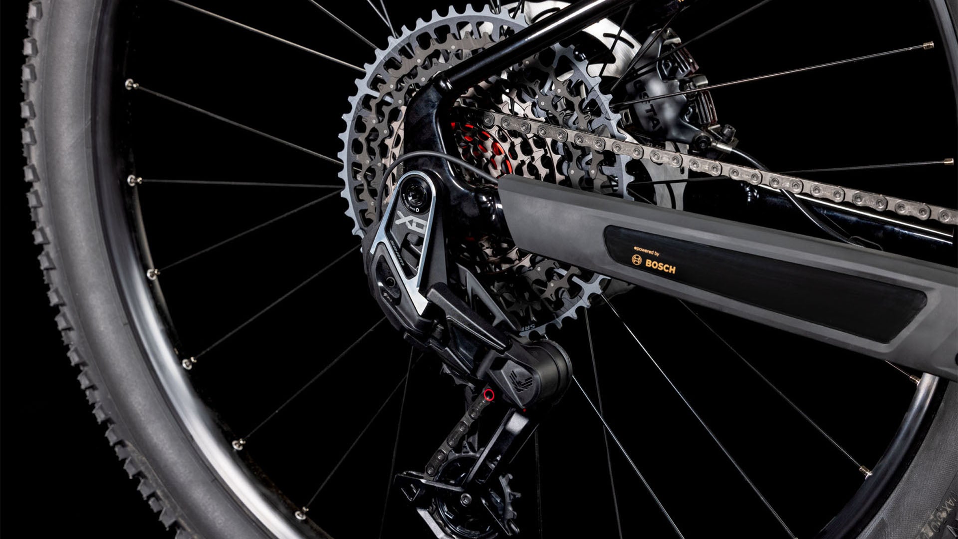 Nahaufnahme des Hinterrads des CUBE Reaction Hybrid SLT 800 solareclipse'n'bronze 2025, der SRAM XO Eagle-Schaltung, der Kette, des Umwerfers und des Bosch CX-Motors vor einem schwarzen Hintergrund.