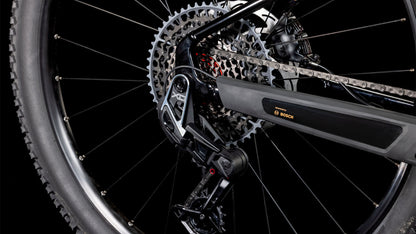 Nahaufnahme des Hinterrads des CUBE Reaction Hybrid SLT 800 solareclipse'n'bronze 2025, der SRAM XO Eagle-Schaltung, der Kette, des Umwerfers und des Bosch CX-Motors vor einem schwarzen Hintergrund.