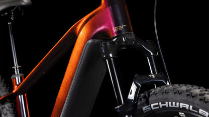 Nahaufnahme der Vorderseite des CUBE Reaction Hybrid SLT 800 solareclipse'n'bronze 2025, die den metallic-orangenen Rahmen, die Federgabel, die Schwalbe-Reifen und die Sram XO Eagle-Getriebedetails vor einem schwarzen Hintergrund hervorhebt.
