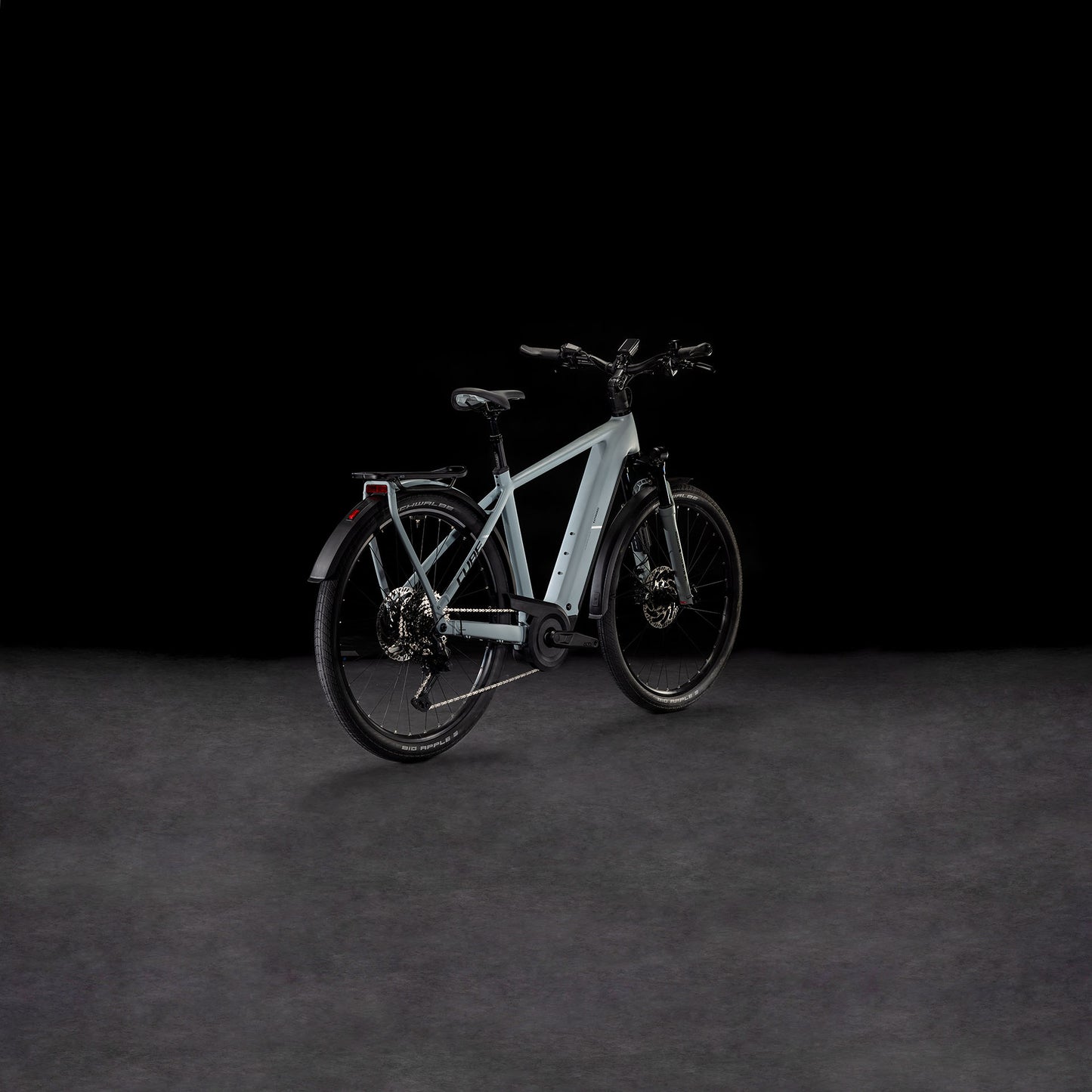 Das CUBE Kathmandu Hybrid EX 800 haze´n´black 2025, ein modernes hellgraues E-Bike mit dicken Reifen, Bosch CX Motor, Gepäckträger und Schutzblechen vorne/hinten, wird auf einer dunklen strukturierten Oberfläche vor schwarzem Hintergrund präsentiert.