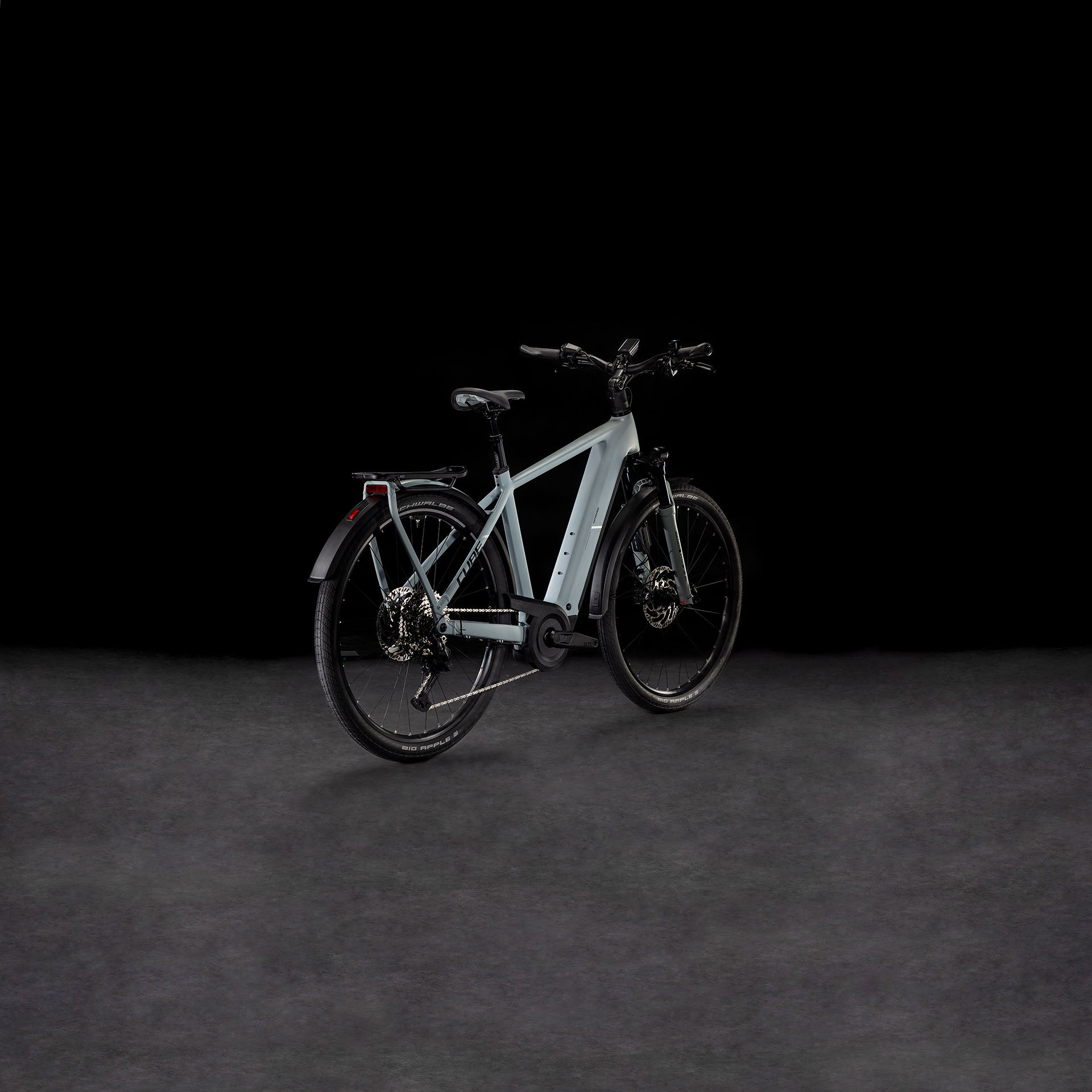 Das CUBE Kathmandu Hybrid EX 800 haze´n´black 2025, ein modernes hellgraues E-Bike mit dicken Reifen, Bosch CX Motor, Gepäckträger und Schutzblechen vorne/hinten, wird auf einer dunklen strukturierten Oberfläche vor schwarzem Hintergrund präsentiert.