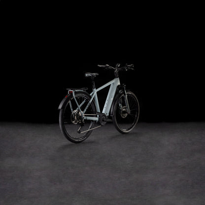 Das CUBE Kathmandu Hybrid EX 800 haze´n´black 2025, ein modernes hellgraues E-Bike mit dicken Reifen, Bosch CX Motor, Gepäckträger und Schutzblechen vorne/hinten, wird auf einer dunklen strukturierten Oberfläche vor schwarzem Hintergrund präsentiert.
