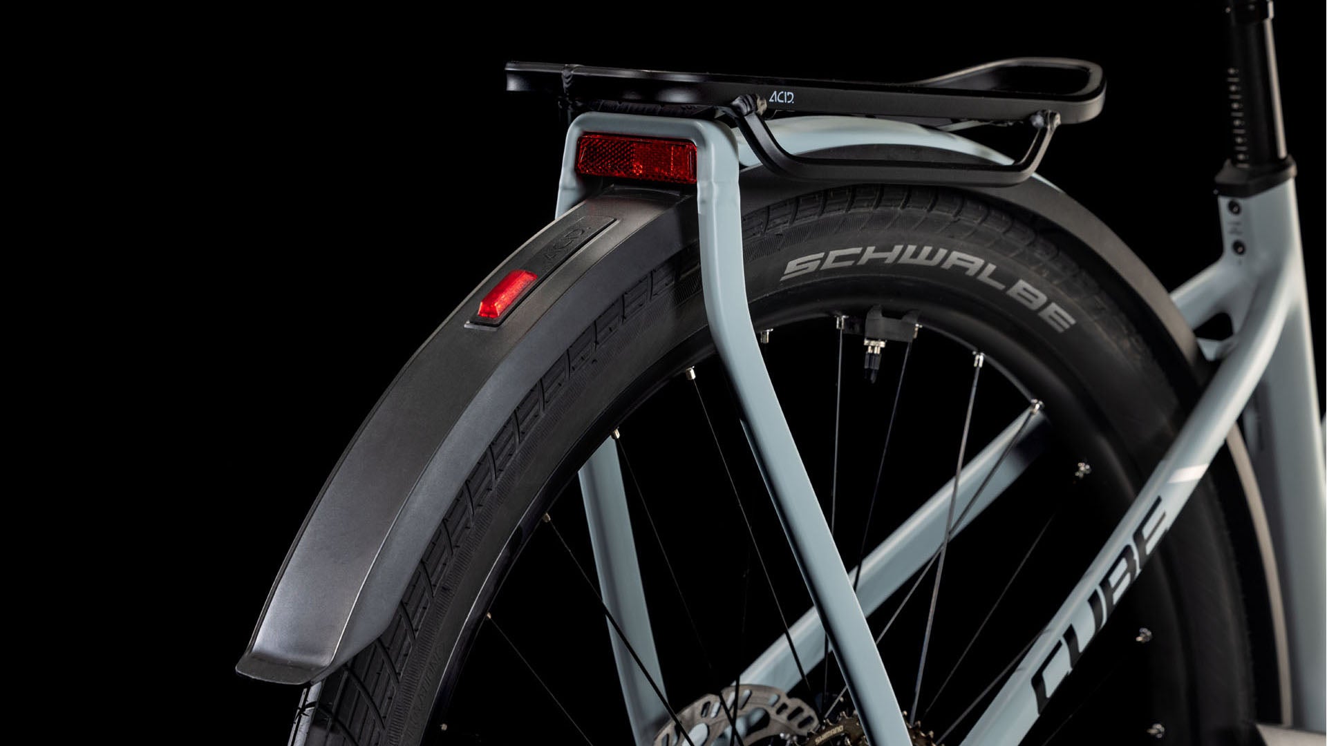 Nahaufnahme des Hinterrads und des Schutzblechs eines hellen CUBE Kathmandu Hybrid EX 800 haze´n´black Trapeze 2025 mit Gepäckträger, rotem Reflektor und sichtbaren Schwalbe-Reifen vor schwarzem Hintergrund.