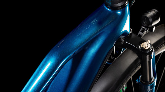 Nahaufnahme des CUBE Kathmandu Hybrid EX 800 electricblue'n'chrome Trapeze 2025 Rahmens. Hervorzuheben sind das glänzende Finish, die sanften Kurven am Oberrohr und die vordere Federgabel vor schwarzem Hintergrund.