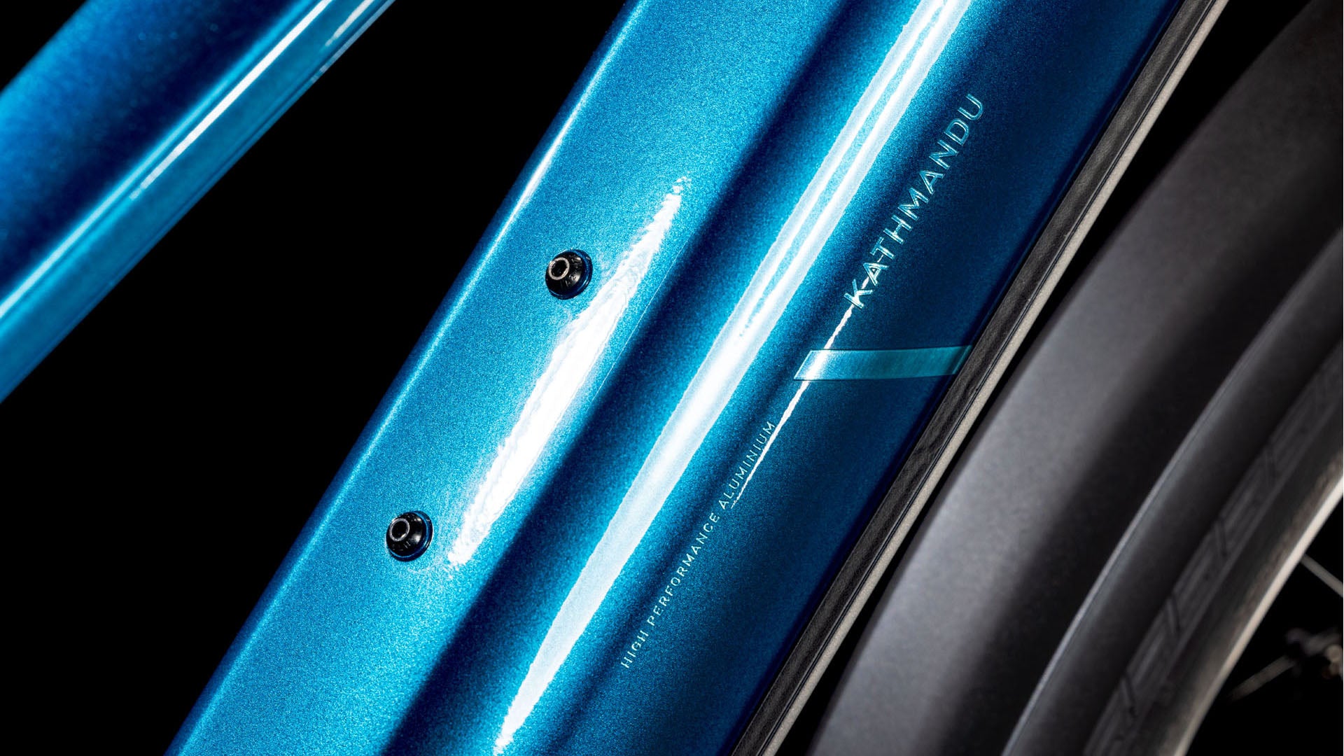 Nahaufnahme des glänzenden Rahmens des CUBE Kathmandu Hybrid EX 800 electricblue'n'chrome Trapeze 2025 mit Schraubenbefestigungen und einem Teil des Reifens. Die Reflexionen heben das metallische Finish hervor - ideal für ein Upgrade mit einem 800 Wh PowerTube Akku oder einem Bosch CX Motor.