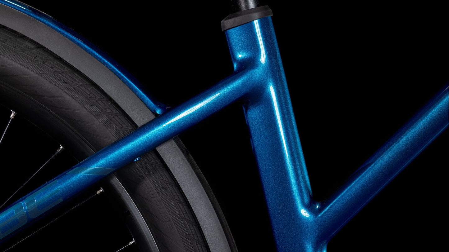 Nahaufnahme des CUBE Kathmandu Hybrid EX 800 electricblue'n'chrome Trapeze 2025 Rahmens mit schwarzem Reifen und Schutzblech vor einem dunklen Hintergrund. Das Bild zeigt die schlanken Linien des Fahrrads, die glänzende Oberfläche und die hochwertige CUBE Handwerkskunst.
