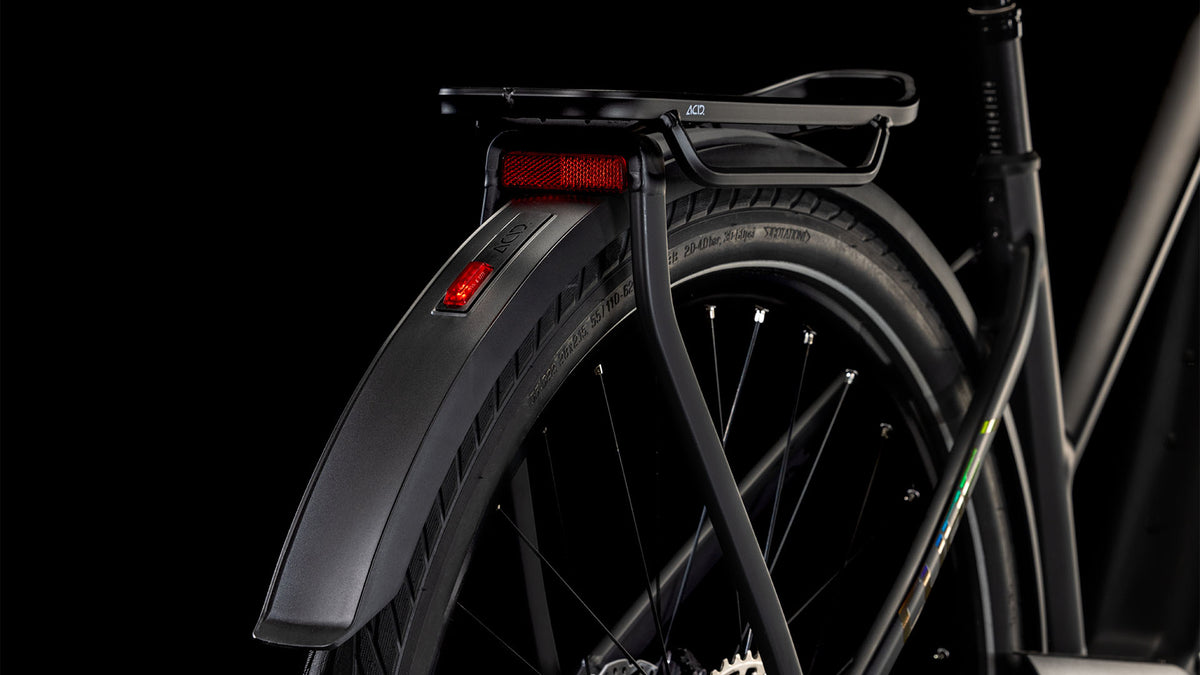 Nahaufnahme des Hinterrads des CUBE Cube Kathmandu Hybrid EXC 800 black'n'prism Trapeze 2025 mit Schutzblech, Gepäckträger, zwei roten Reflektoren und einer Shimano XT Schaltung vor schwarzem Hintergrund.