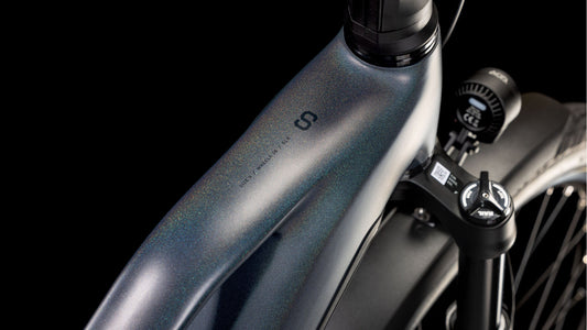 Nahaufnahme des Metallrahmens und der Vorderradaufhängung des CUBE Kathmandu Hybrid Comfort SLX 800 nightsky´n´ink Trapeze 2025. Zu sehen sind schillernde Lackierung, Bosch CX-Motor, Scheinwerfer und die detaillierte Konstruktion von CUBE vor einem schwarzen Hintergrund.