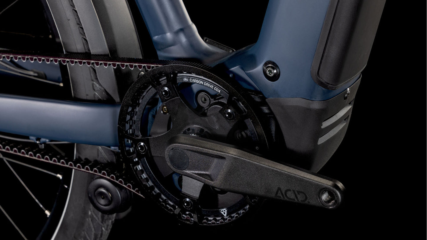 Nahaufnahme der Kurbelgarnitur und des Riemenantriebssystems des CUBE Kathmandu Hybrid Comfort SLX 800 nightsky´n´ink Trapeze 2025, die den mit ACID gekennzeichneten Pedalarm, die Zahnräder, das Hinterrad und die Kompatibilität mit der Enviolo-Nabenschaltung zeigt.