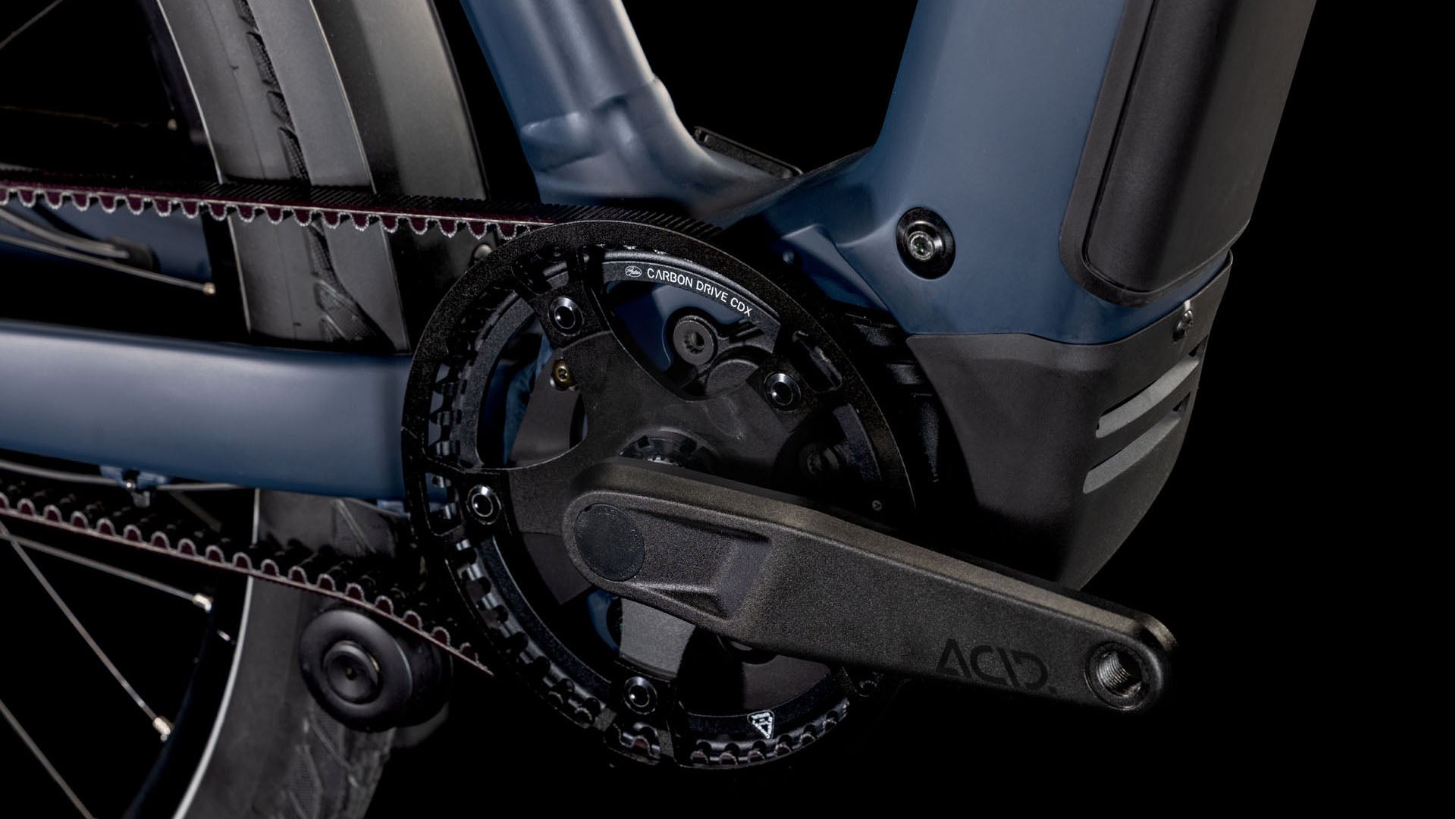 Nahaufnahme der Kurbelgarnitur und des Riemenantriebssystems des CUBE Kathmandu Hybrid Comfort SLX 800 nightsky´n´ink Trapeze 2025, die den mit ACID gekennzeichneten Pedalarm, die Zahnräder, das Hinterrad und die Kompatibilität mit der Enviolo-Nabenschaltung zeigt.