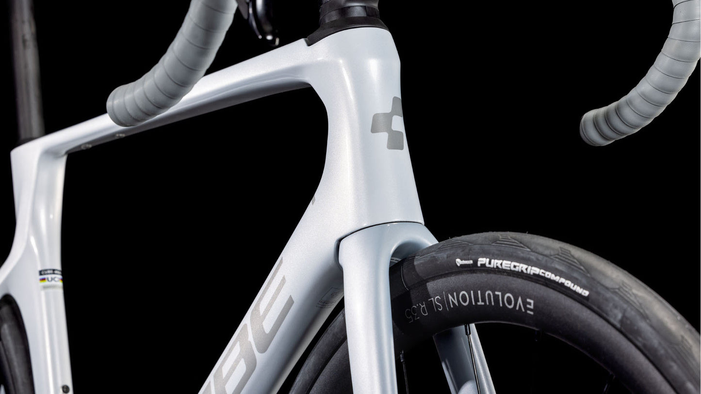 Nahaufnahme des Vorderrahmens, der Gabel und des Lenkers des CUBE Agree C:62 ONE foggrey'n'grey 2025 mit einem Reifen, der mit "EVOLUTION SL" und "PUREGRIP Compound" beschriftet ist; Shimano 105 Di2-Teile sind dezent vor einem schwarzen Hintergrund zu sehen.