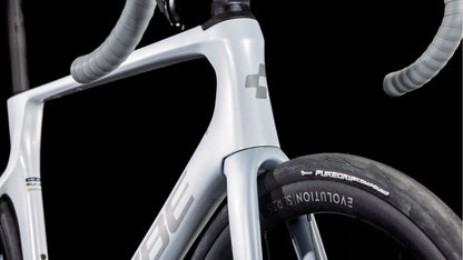 Nahaufnahme des Vorderrahmens, der Gabel und des Lenkers des CUBE Agree C:62 ONE foggrey'n'grey 2025 mit einem Reifen, der mit "EVOLUTION SL" und "PUREGRIP Compound" beschriftet ist; Shimano 105 Di2-Teile sind dezent vor einem schwarzen Hintergrund zu sehen.
