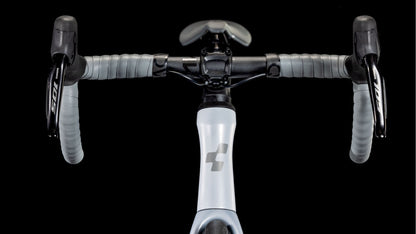 Nahaufnahme der Vorderseite des CUBE Agree C:62 ONE foggrey'n'grey 2025 Lenker und Vorbau vor schwarzem Hintergrund. Zu sehen sind umwickelte Bänder, Shimano 105 Di2 Bremshebel und der Fahrradrahmen mit stilisiertem Branding.