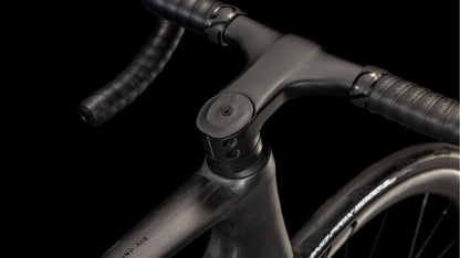 Nahaufnahme des Cube Litening AIR C:68X Race blackline 2025 von CUBE, die den aerodynamischen Lenker, den Vorbau und das Vorderrad vor einem schwarzen Hintergrund zeigt. Der Carbon-Rahmen sieht mit dem schwarzen, mit Tape umwickelten Lenker schlank und modern aus.