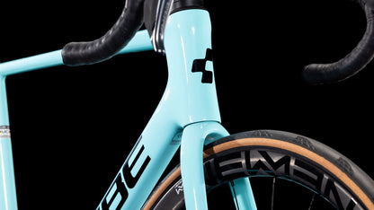 Nahaufnahme der hellblauen Vorderseite eines CUBE Litening AIR C:68X Race dazzle'n'black 2025 Rennrads mit Carbonrahmen-Lenker, Steuerrohr mit schwarzem Logo und hellbraunem Laufrad mit ELEMENT-Branding vor schwarzem Hintergrund.