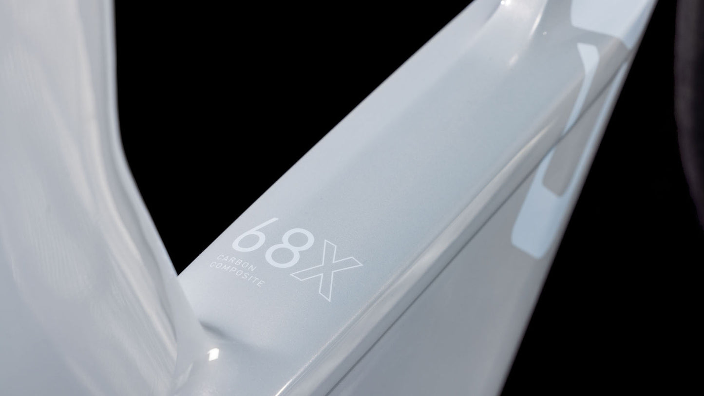 Nahaufnahme einer hellgrauen, glänzenden Oberfläche mit der Aufschrift "68X Carbon Composite" in Weiß auf Schwarz - Teil des CUBE Aerium C:68X Race foggrey'n'white 2026 Triathlonrads.