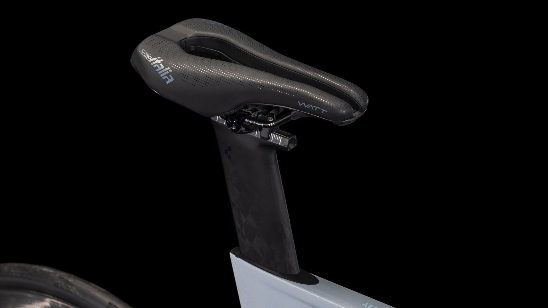 Nahaufnahme eines schwarzen aerodynamischen Sattels auf dem CUBE Aerium C:68X Race foggrey'n'white 2026 Triathlonrad mit Kohlefaser-Sattelstütze und Shimano Ultegra Di2, vor schwarzem Hintergrund. Das Hinterrad ist am linken Rand teilweise sichtbar.