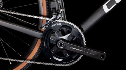 Nahaufnahme eines CUBE Cross Race C:62 Pro carbon'n'orange 2025 Antriebssystems mit schwarzer ROTOR Kurbelgarnitur, Kettenblatt, Shimano 105 Di2 Kette auf mattschwarzem und orangefarbenem Carbonrahmen, hellbraune Reifen vor schwarzem Hintergrund.