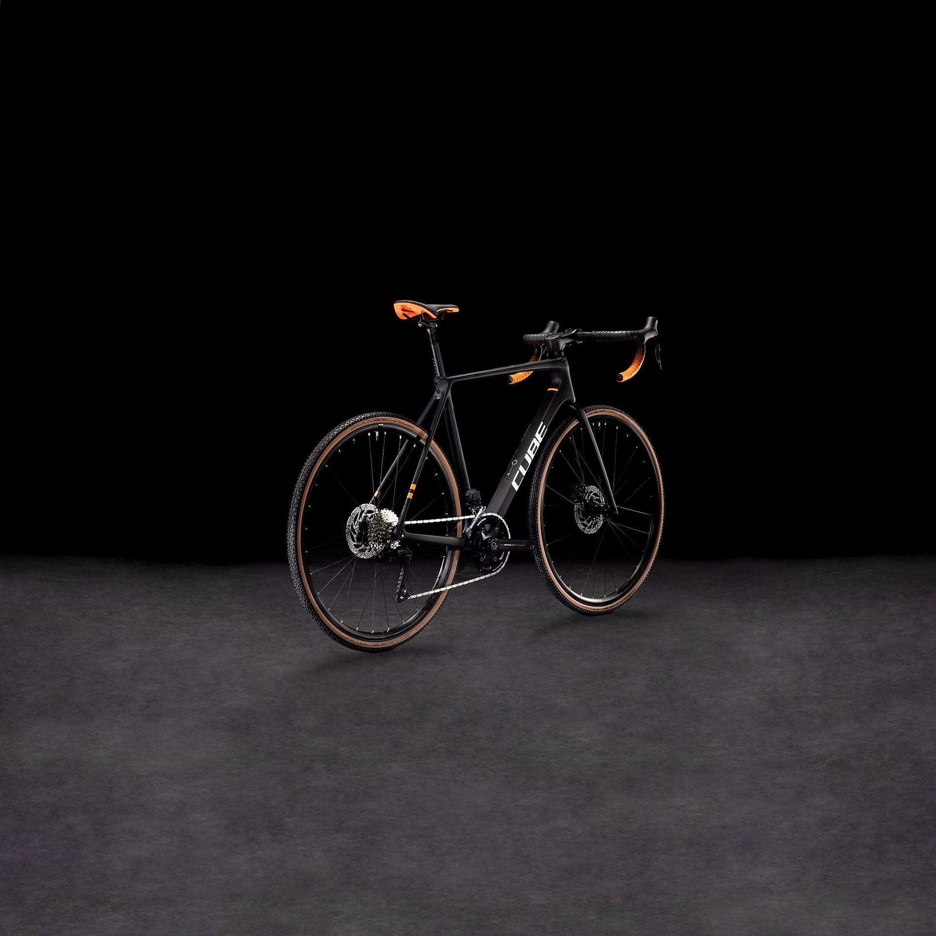 Das CUBE Cross Race C:62 Pro carbon'n'orange 2025 Rennrad mit Carbonrahmen und auffälligen orangefarbenen Akzenten wird vor einem dunklen Hintergrund präsentiert, um sein modernes, aerodynamisches Design zu unterstreichen.