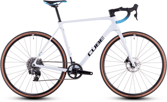 Das CUBE Cross Race C:62 Race polarwhite'n'blue 2025 ist ein Cyclocross-Rad mit schwarzen und blauen Akzenten, Sram Rival AXS, abnehmbarem Lenker, Scheibenbremsen und hellbraunen Seitenwandreifen. Abgebildet in der Seitenansicht auf weißem Hintergrund.