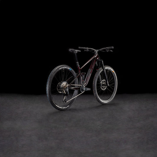 Ein CUBE Stereo ONE44 C:68X SLX 29 liquidviolet'n'black 2026 Mountainbike mit robuster Bereifung ist auf einer dunklen, strukturierten Oberfläche vor schwarzem Hintergrund abgebildet, schräg gestellt, um sein hinteres und seitliches Profil hervorzuheben.