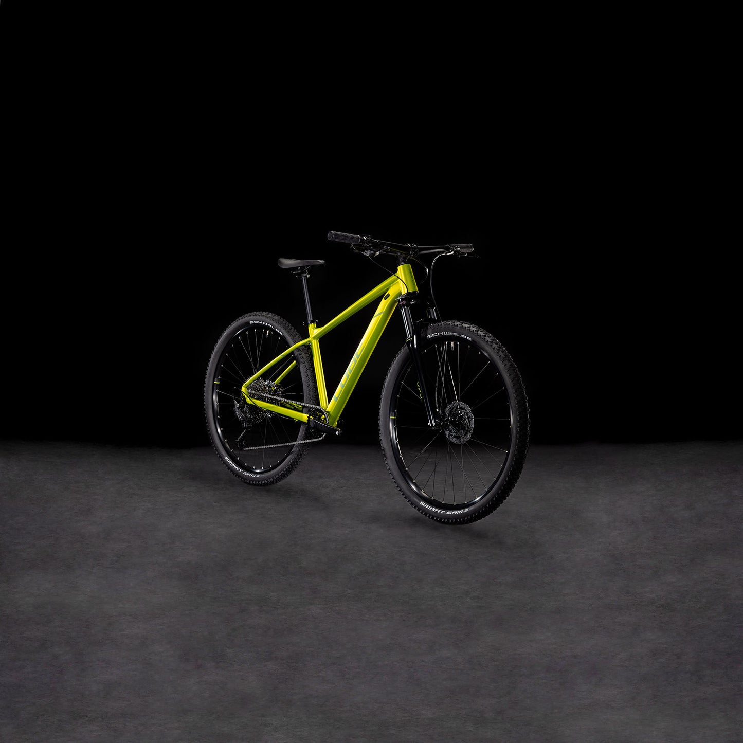 Ein Cube Aim SLX Flashlime´n´Juniper 2025 Mountainbike von CUBE, mit 11-fach Cues Schaltung, schwarzem Lenker, Rädern und Sattel, wird auf einer dunklen strukturierten Oberfläche mit schwarzem Hintergrund präsentiert.