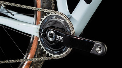 Nahaufnahme einer SRAM XX SL Eagle Transmission-Kurbelgarnitur mit Kettenblatt, Kette und XX SRAM-Kurbelarm an einem weißen CUBE Phenix C:68X SLT teamline 2025-Rahmen, wobei ein Teil des Hinterreifens zu sehen ist.