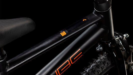 Nahaufnahme eines CUBE Numove 120 RT black'n'orange 2025 Rahmens mit orangem Schriftzug, der den Sitz, das Oberrohr und einen Teil des Hinterrads vor einem schwarzen Hintergrund zeigt.