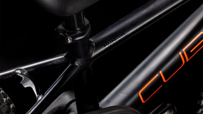 Nahaufnahme eines Cube Numove 120 RT black'n'orange 2025 Rahmens mit Sattelstütze, einem Teil des Hinterreifens und CUBE in Orange. Hervorzuheben sind das schlanke Design und die zuverlässige Bremsleistung, ideal für junge Radfahrer.