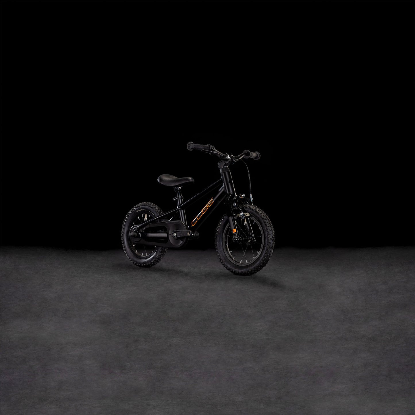 Das CUBE Numove 120 RT black'n'orange 2025, ein kleines Kinderfahrrad mit Stützrädern, grobstolligen Reifen, niedrigem Rahmen und Felgenbremse für sicheres Anhalten, steht mittig vor einem dunklen Hintergrund.
