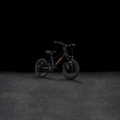 Das CUBE Numove 120 RT black'n'orange 2025, ein kleines Kinderfahrrad mit Stützrädern, grobstolligen Reifen, niedrigem Rahmen und Felgenbremse für sicheres Anhalten, steht mittig vor einem dunklen Hintergrund.