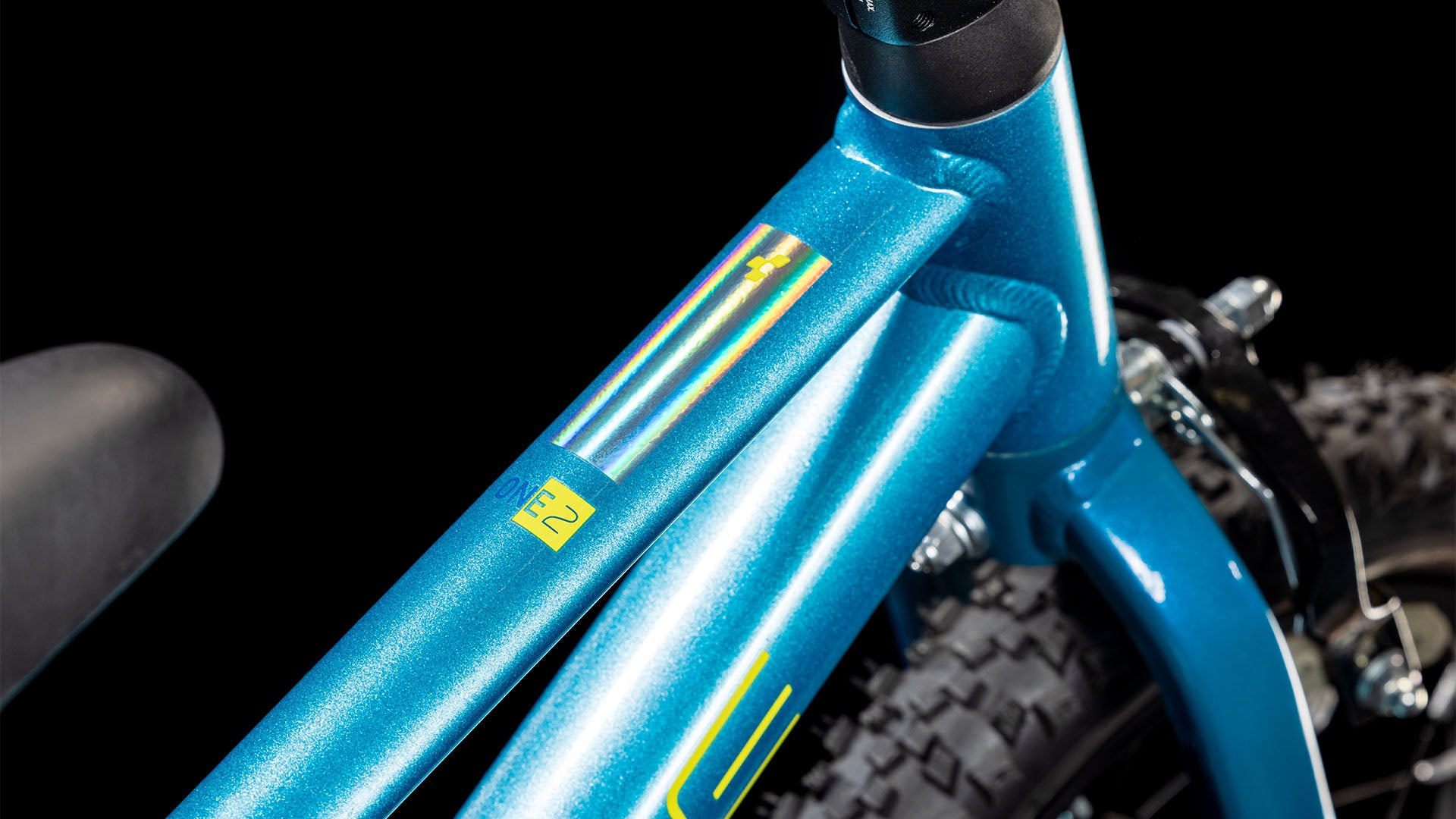 Nahaufnahme eines CUBE Cube Numove 120 RT blue'n'lime 2025 Fahrrads mit Aluminiumrahmen, das einen gelben Aufkleber mit der Nummer 2 und mehrfarbigen Streifen zeigt. Ein Teil des Hinterreifens und des Sitzes sind vor einem schwarzen Hintergrund zu sehen.
