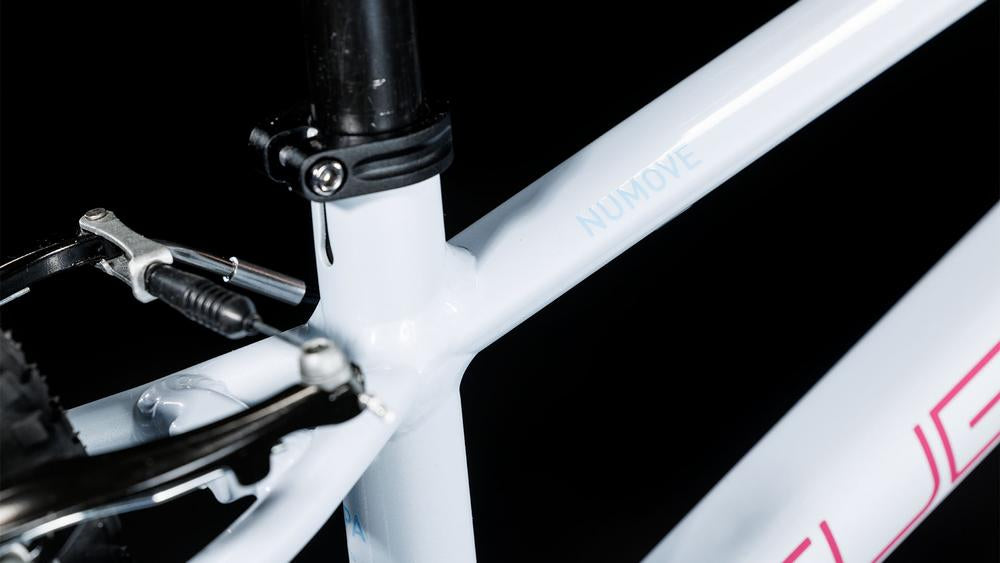 Nahaufnahme des CUBE Numove 140 flashwhite'n'pink 2025 Rahmens mit kindgerechten V-Brakes, die das Sitzrohr, die Hinterradbremse und NUMOVE auf der Rahmenbauweise von CUBE vor einem schwarzen Hintergrund zeigt.