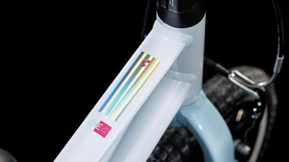 Nahaufnahme des CUBE Numove 140 flashwhite'n'pink 2025 Rahmens mit seinem einzigartigen Aufbau mit holographischem Aufkleber und rotem ONE E4 Label. Das Bild zeigt auch einen Teil des Vorderreifens, den Bremszug und die kinderfreundlichen V-Brakes von CUBE.