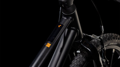 Nahaufnahme des Vorderrahmens und des Laufrads des CUBE Numove 180 black'n'orange 2025 mit schlankem Design, Schwalbe-Reifen, einem kleinen orangefarbenen Logo und Etikett auf dem 6061-Aluminiumrahmen vor einem dunklen Hintergrund.