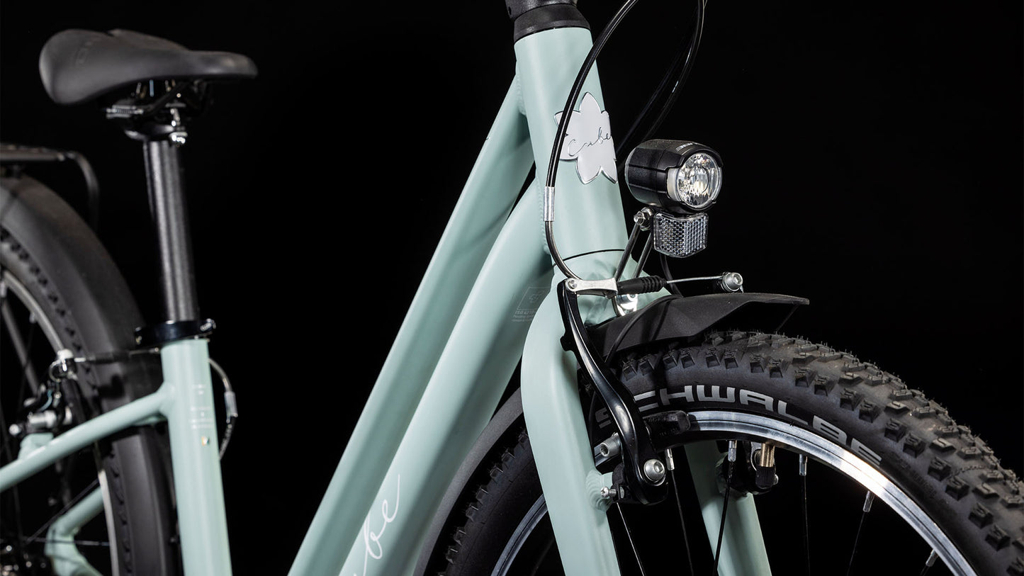 Nahaufnahme des CUBE Ella 240 aloegreen'n'white 2025 von CUBE, mit Lenker, Vorderrad mit Schwalbe-Reifen, Shimano-Schaltung, Scheinwerfer und Schutzblech vor schwarzem Hintergrund.