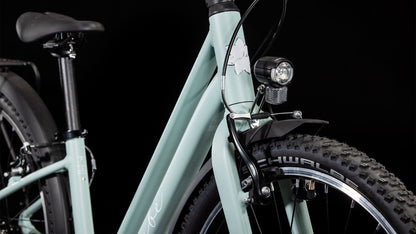 Nahaufnahme des CUBE Ella 240 aloegreen'n'white 2025 von CUBE, mit Lenker, Vorderrad mit Schwalbe-Reifen, Shimano-Schaltung, Scheinwerfer und Schutzblech vor schwarzem Hintergrund.